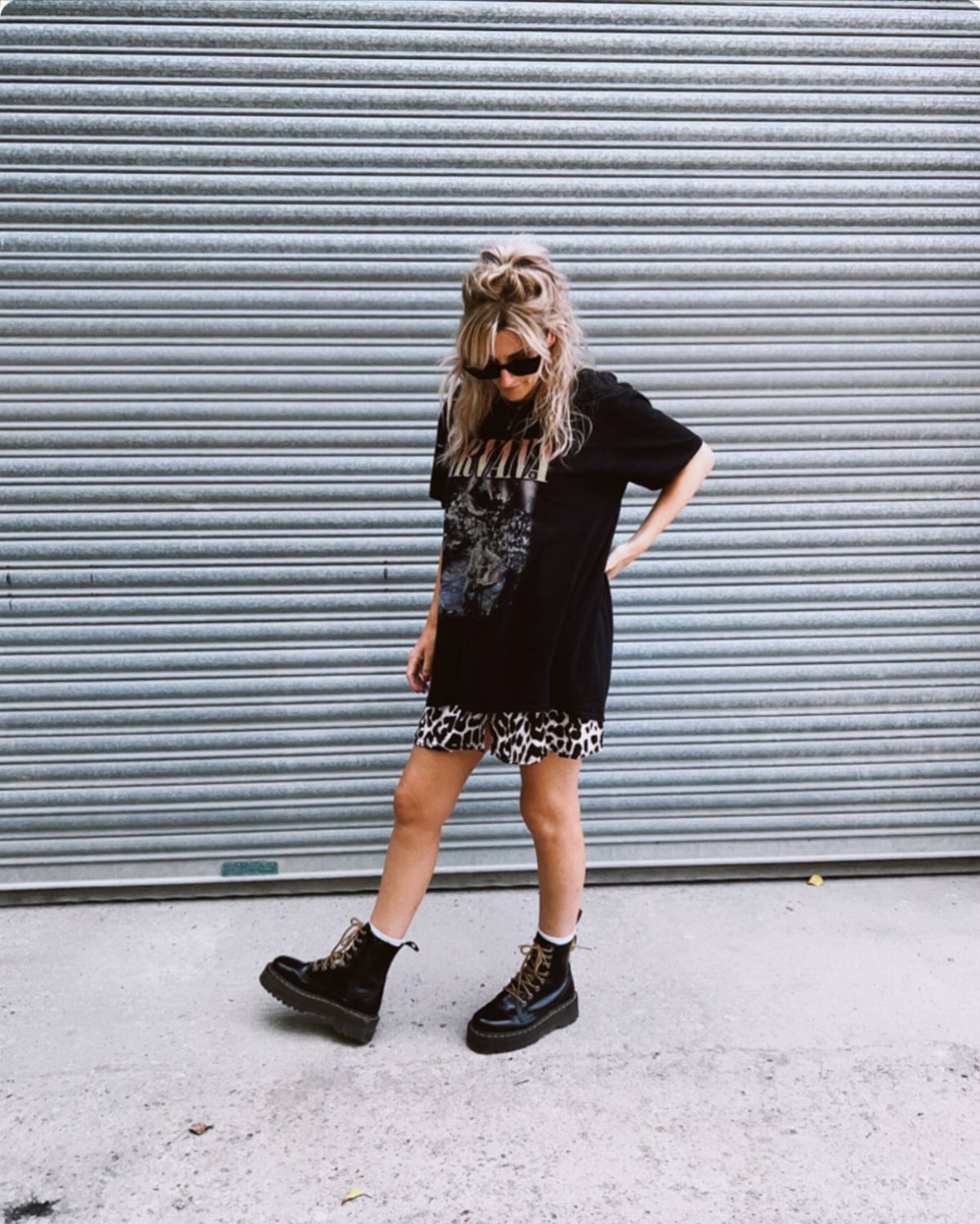 Woman wearing oversized black graphic tee, leopard print skirt, and black combat boots.