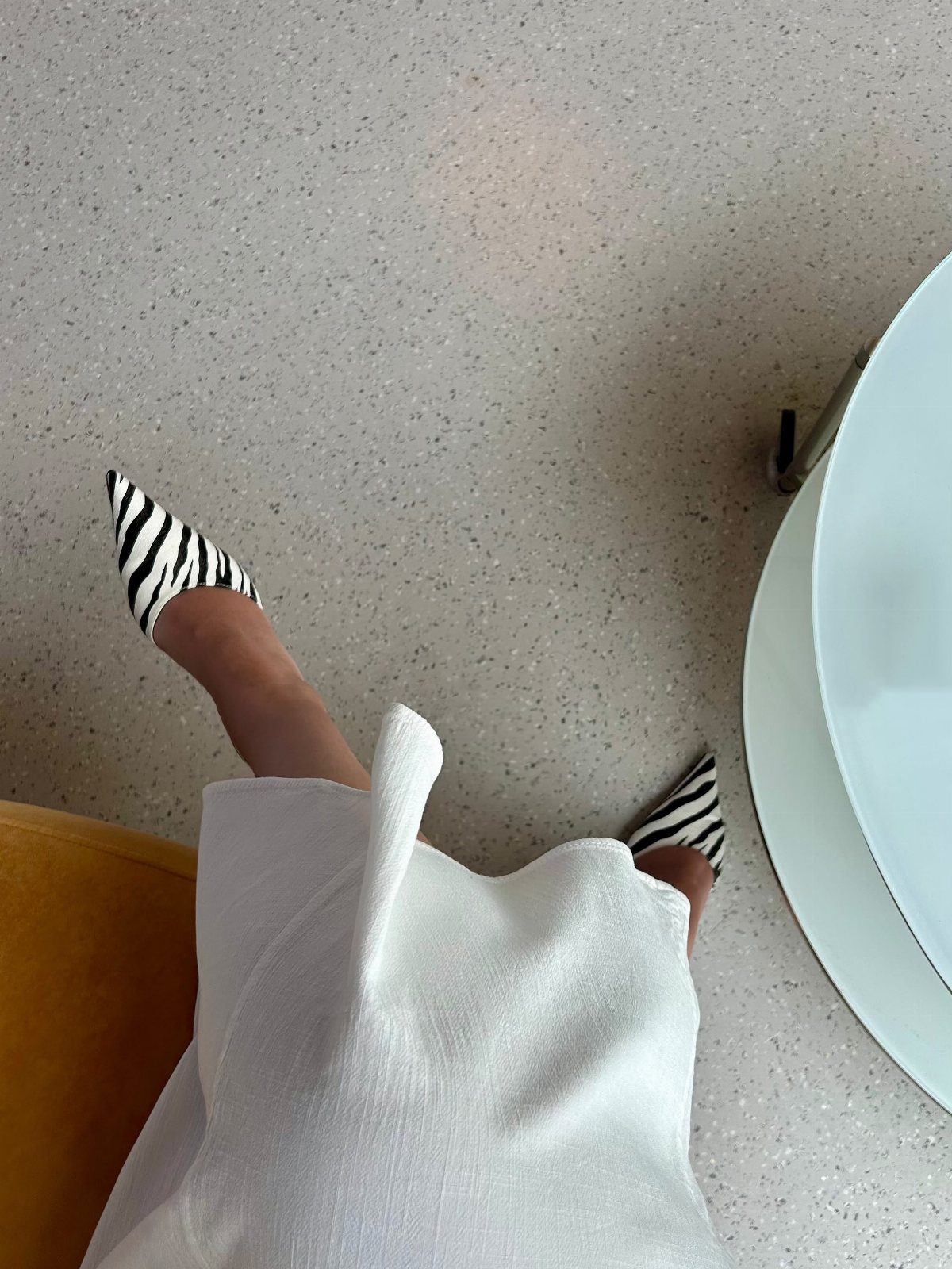 Zebra Kitten Heels: 7 Styles from Slingbacks to Mules 5 Zebra print kitten heels worn with a white outfit on a speckled floor.